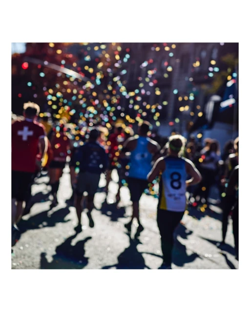 Marathon runners in athletic wear race on city street with confetti; crowd of athletes participating in running event outdoors.