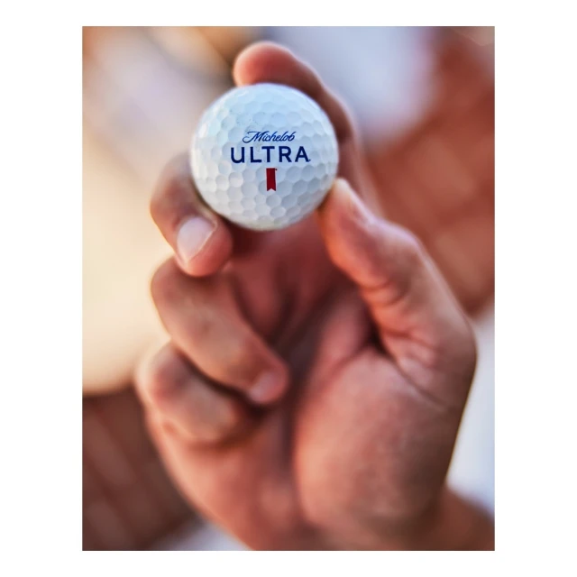 Close-up shot of a person holding a Michelob Ultra golf ball, showcasing the product logo and the textures of the ball and the hand.
