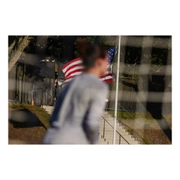 Out of focus person in foreground with a flying American flag and outdoor staircase in background photographed by Pete Thompson