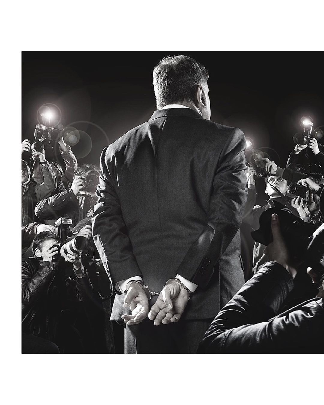 Rear view of an adult male in a suit being escorted by paparazzi and photographers in handcuffs. Dark, monochromatic and formal.
