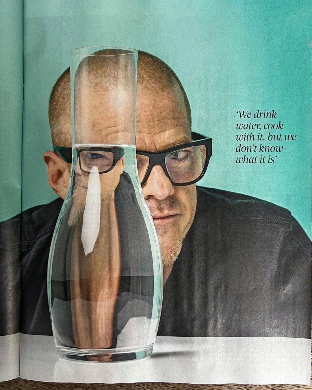 Close-up shot of a bald adult male with glasses peering behind a clear glass pitcher filled with water, in a studio setting with text.
