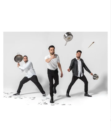 Three men in white shirts and black pants pose with cooking pots and utensils in a studio with a white background and scattered white papers.