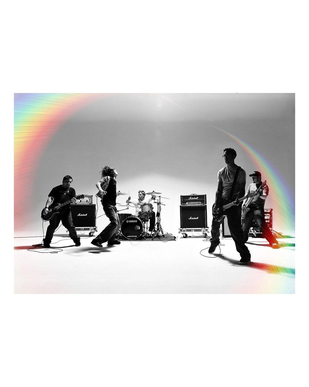 Five-piece rock band performing in a white studio framed by a glowing holographic rainbow arch overhead, photographed by Perou.