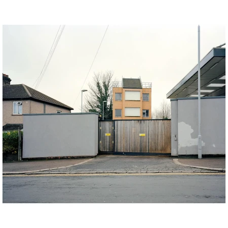 Suburban scene featuring residential architecture with a wooden gate in the foreground, creating a sense of depth and enclosure.