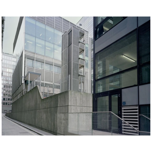 Exterior view of modern architecture featuring a gray concrete structure and reflective glass buildings in an urban environment.
