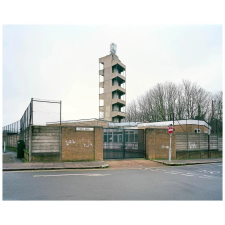 Exterior of concrete tower and brick building with graffiti, metal fence, and street sign on overcast day in urban setting.