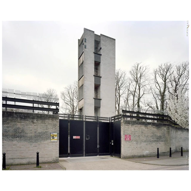 Exterior shot of a tall, concrete building with a gated entrance, surrounded by trees and a gray sky, creating an architectural image.
