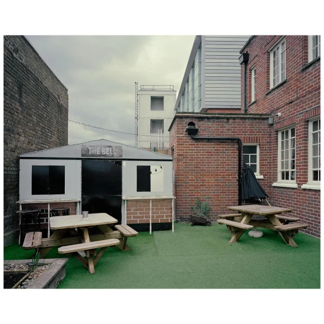 Outdoor patio area with picnic tables and a gray building labeled 'The Bell' against a backdrop of brick and modern architecture.
