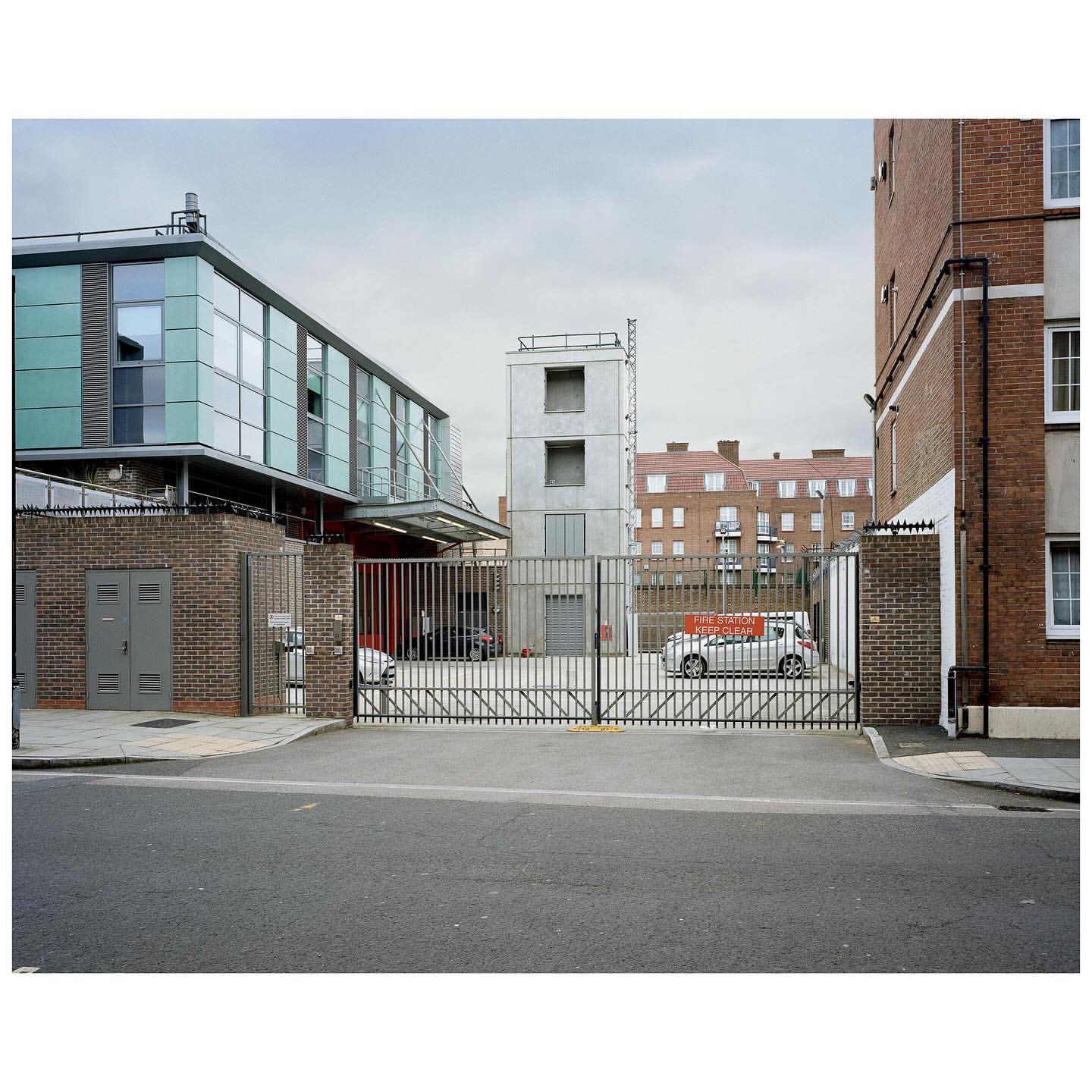Exterior view of modern architecture featuring a gray brick building, glass facade, and metal gate in an urban environment under an overcast sky.