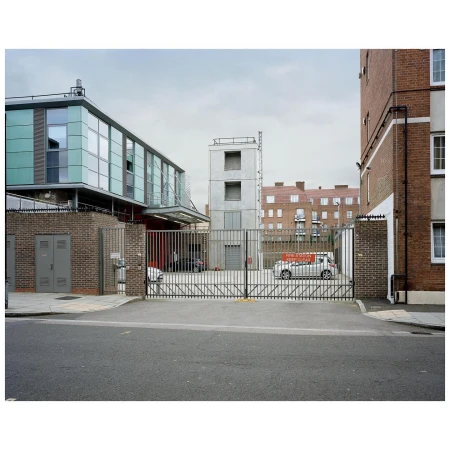 Exterior view of modern architecture featuring a gray brick building, glass facade, and metal gate in an urban environment under an overcast sky.