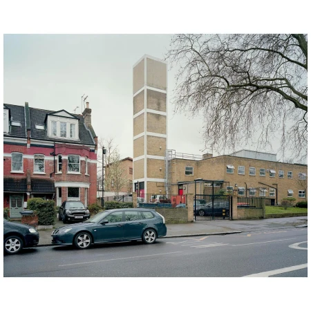 Urban scene featuring a tall, rectangular tower alongside a multi-story brick building and parked cars on a quiet, overcast day.