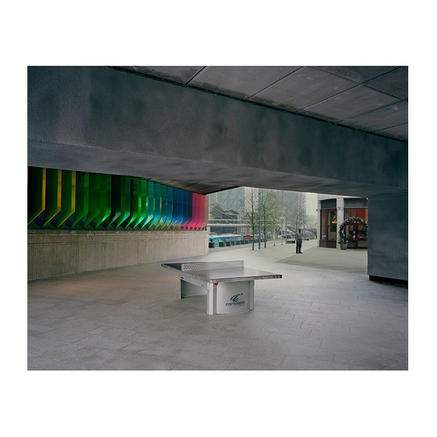 Exterior shot of a concrete plaza with a ping pong table under a concrete structure, bright colorful wall art behind the table.