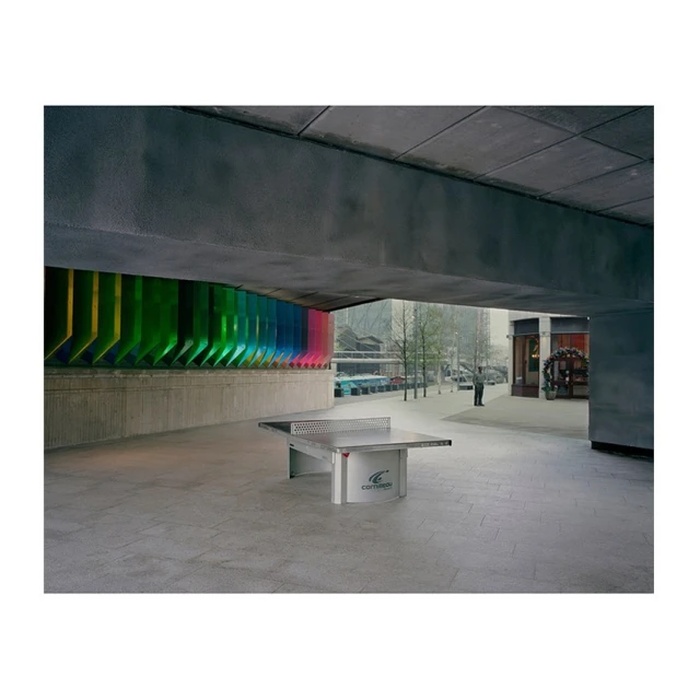 Exterior shot of a concrete plaza with a ping pong table under a concrete structure, bright colorful wall art behind the table.
