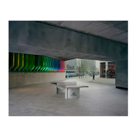 Exterior shot of a concrete plaza with a ping pong table under a concrete structure, bright colorful wall art behind the table.