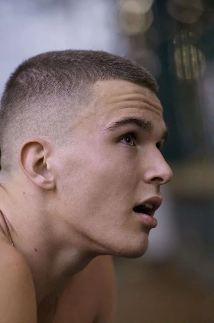 Close-up shot of a young adult male with a short haircut, looking up with an open mouth in an indoor setting, focusing on his face and expression.