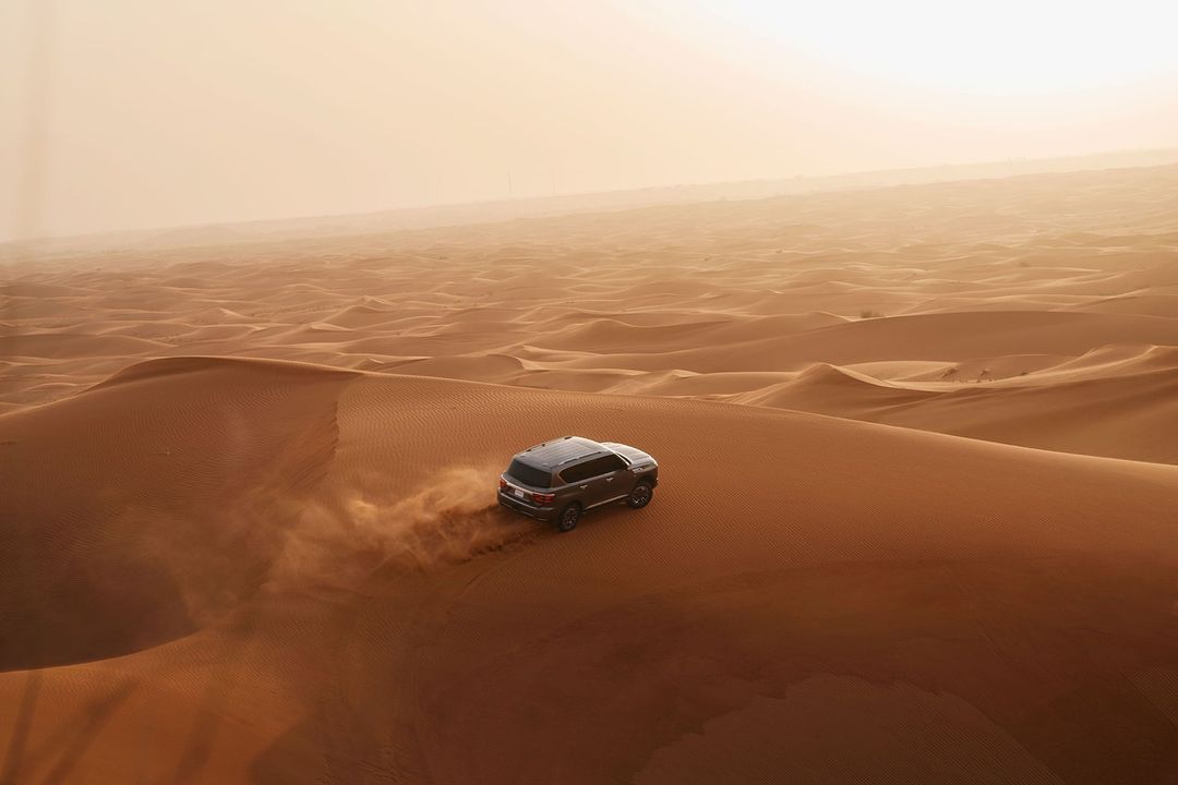SUV vehicle driving on sand dunes in desert environment with warm sunny light and sandy color palette, transport, landscape photography.