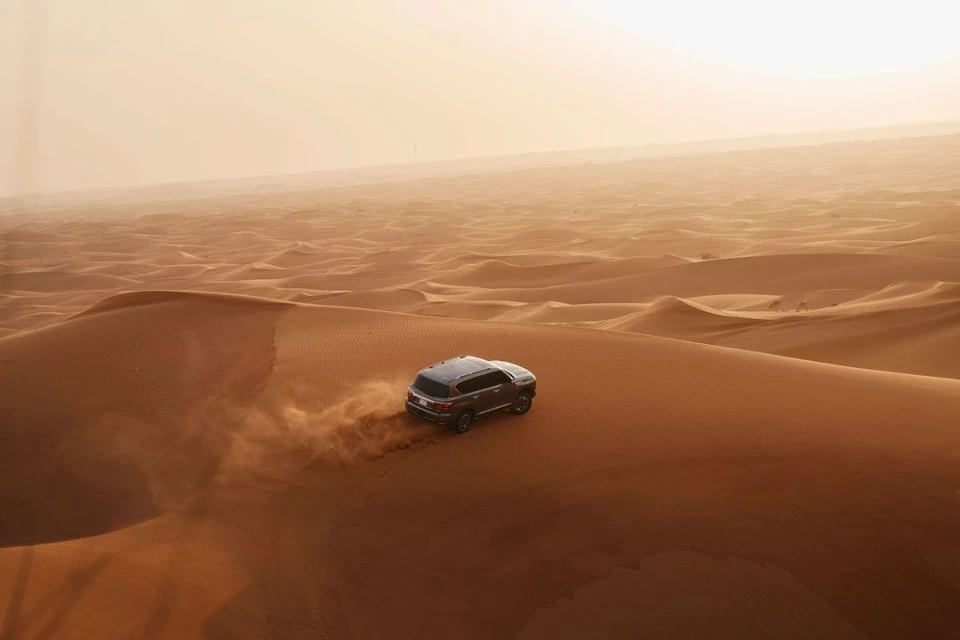 SUV vehicle driving on sand dunes in desert environment with warm sunny light and sandy color palette, transport, landscape photography.