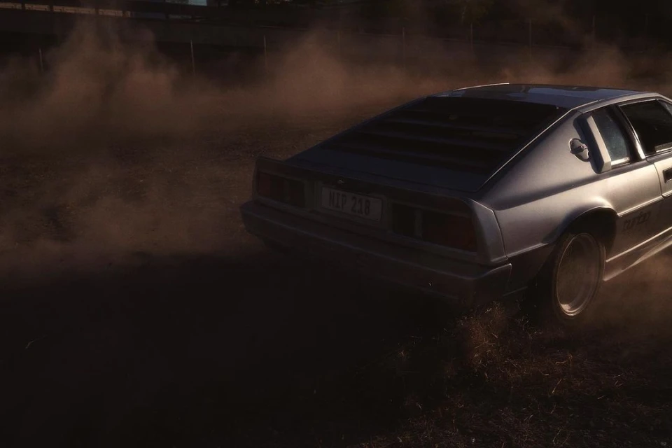 Silver Lotus sports car drifting and kicking up dust on a dirt surface, bathed in warm, sunset-like lighting.