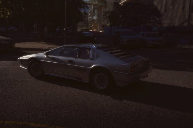 Silver Lotus Esprit Turbo parked on a city street with a dark background and a contemporary building during daylight hours.