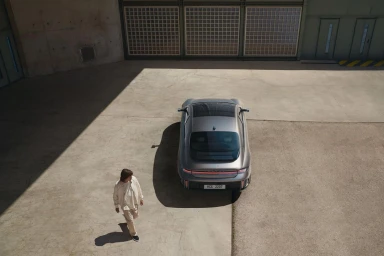 High-angle shot of a grey sports car parked in an industrial courtyard with a person walking nearby.