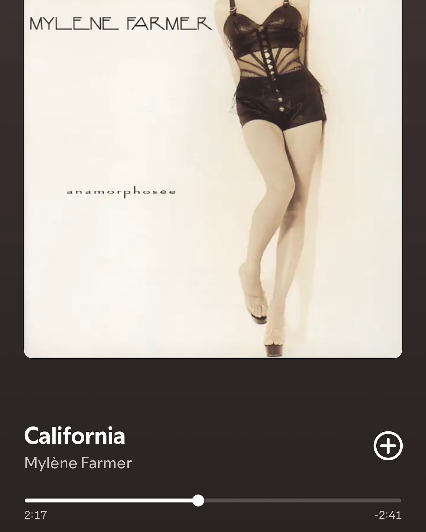 Mylene Farmer poses in a black bodysuit and high heels against a bright white backdrop for the 'Anamorphosée' album cover.