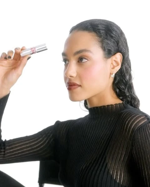 Woman holding silver lipstick tube in a studio setting with a clean, bright background, wearing a black top, looking off to the side.