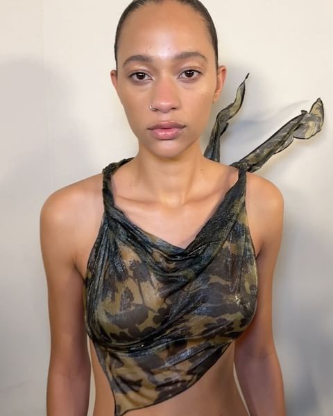 Adult female portrait with fair skin and a nose ring poses in a sheer camouflage halter top against a neutral backdrop.