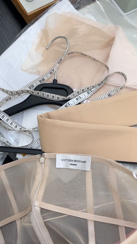 Close-up on a Victoria Beckham garment with hanger, measuring tape, and fabric, showcasing fashion design and garment construction.