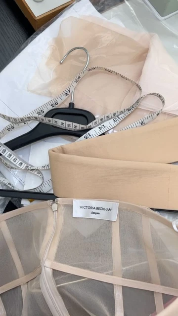 Close-up on a Victoria Beckham garment with hanger, measuring tape, and fabric, showcasing fashion design and garment construction.