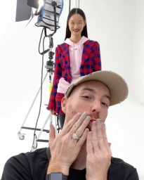 Man wearing a cap blowing a kiss with a woman standing in the background in a studio