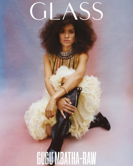 Gugu Mbatha-Raw sits in an off-white tulle dress and black boots, on a pink background. She is featured on the cover of GLASS magazine.