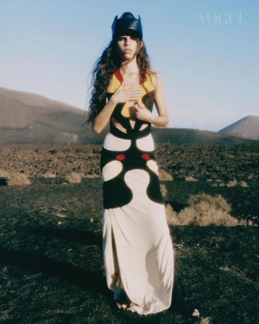 Fashion editorial shot of a woman in a black and white dress and a unique headpiece, standing in a barren, mountainous landscape.