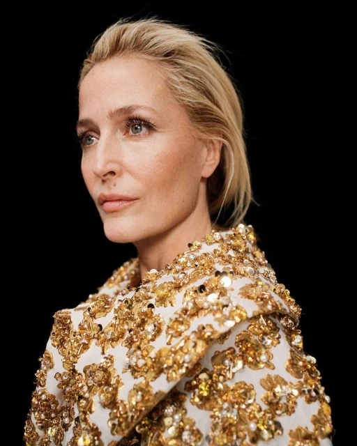 Close-up portrait of a blonde woman in a white and gold sequined top against a black background, capturing a sophisticated and elegant look.