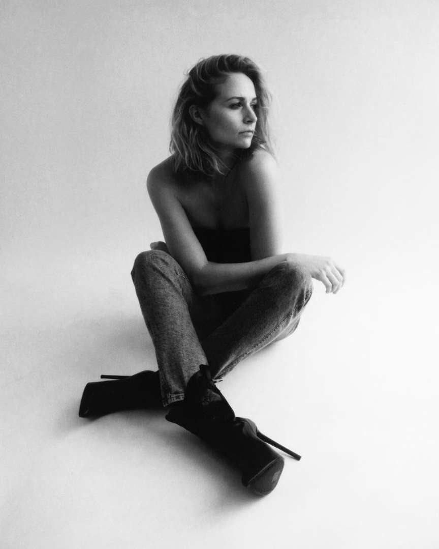 Monochrome portrait of a woman seated on a white floor wearing jeans and high heel boots