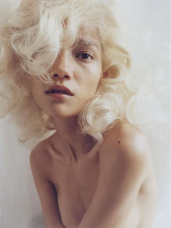 Portrait of a woman with voluminous blonde curly hair against a light background by photographer Nick Thompson.