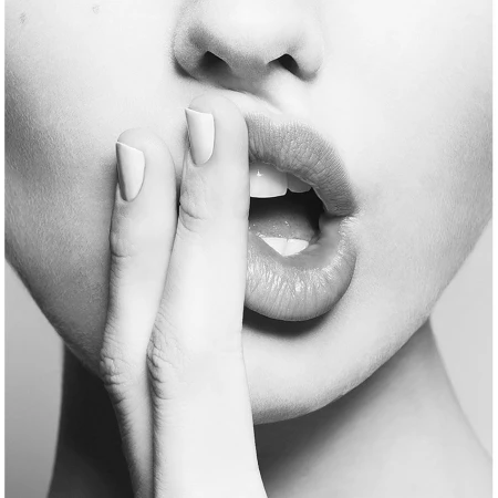 Close-up monochrome portrait of a person holding two fingers near their parted lips, showing manicured nails.