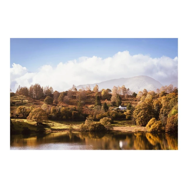 Scenic view of a tranquil lake reflecting the surrounding hills covered with autumn trees under a cloudy sky, creating a serene landscape.