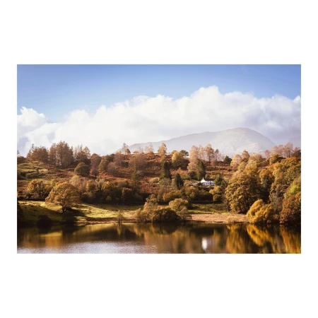 Scenic view of a tranquil lake reflecting the surrounding hills covered with autumn trees under a cloudy sky, creating a serene landscape.