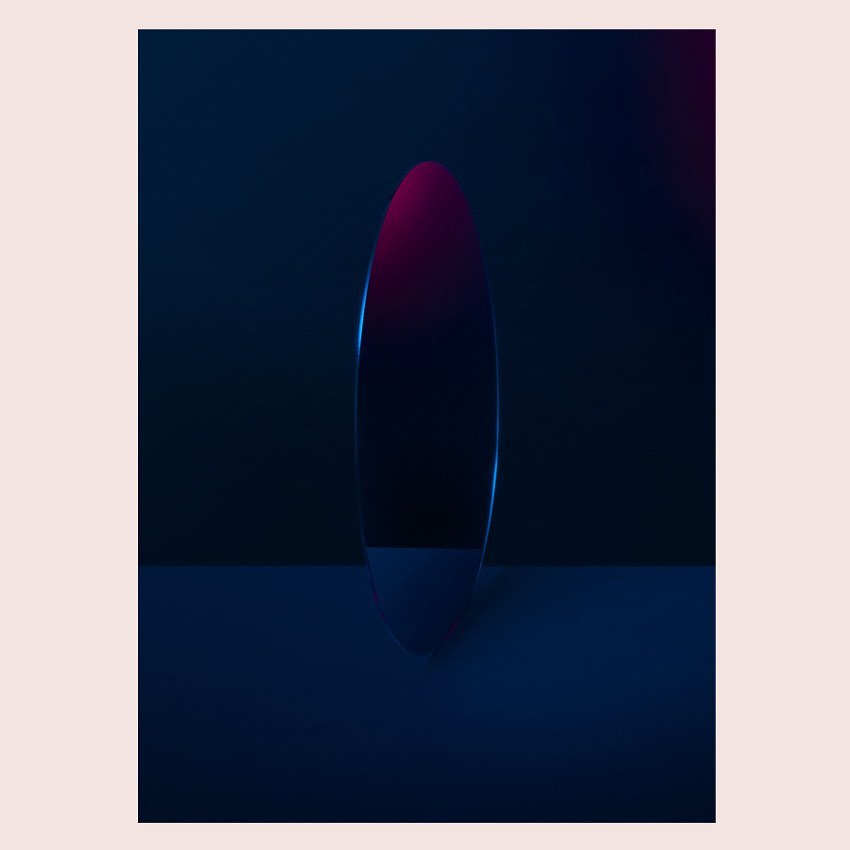 Abstract shot of reflective oval against a dark background with subtle pink and blue light reflecting on the surface.