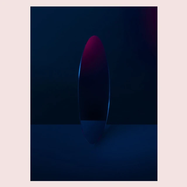 Abstract shot of reflective oval against a dark background with subtle pink and blue light reflecting on the surface.