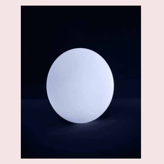 Minimalist product shot of a glowing white spherical lamp against a dark backdrop, highlighting its smooth texture and simple design.