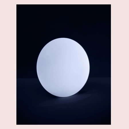 Minimalist product shot of a glowing white spherical lamp against a dark backdrop, highlighting its smooth texture and simple design.