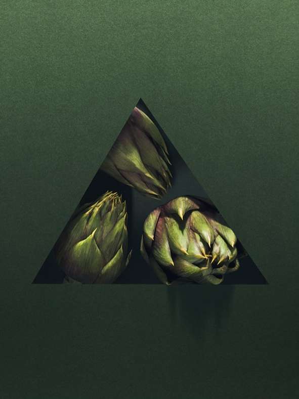 Three artichokes are positioned within a triangle cut out of a dark green surface, casting a shadow that enhances the composition.
