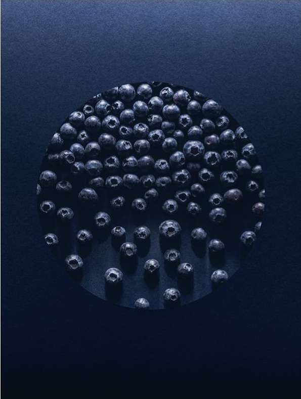 Overhead shot of blueberries arranged in a circle pattern on a blue background creating an abstract, colorful food still life.