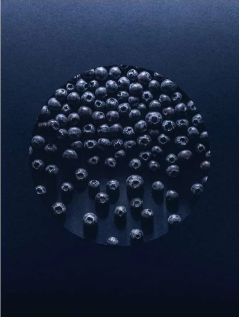 Overhead shot of blueberries arranged in a circle pattern on a blue background creating an abstract, colorful food still life.