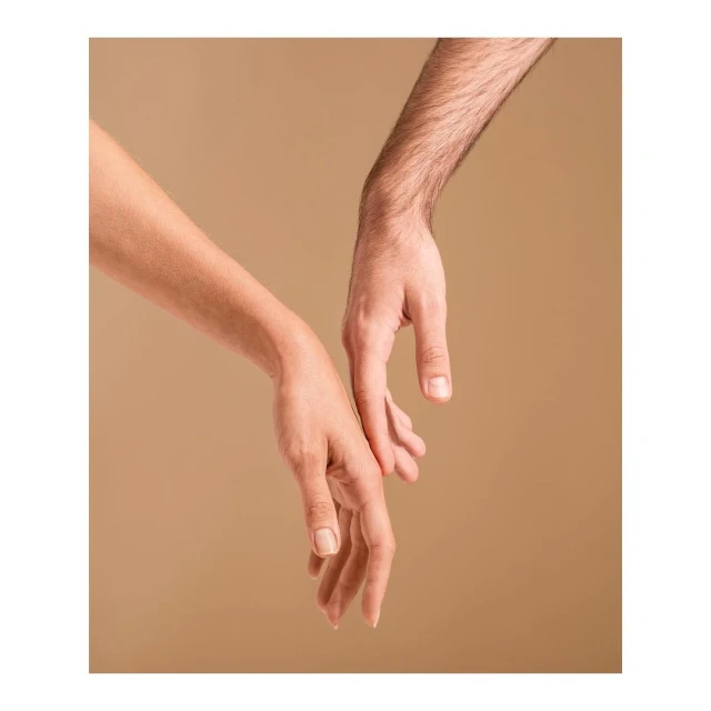 Close-up of a woman's arm and a man's arm reaching towards each other on a neutral background, conveying a sense of connection and intimacy.