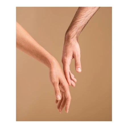 Close-up of a woman's arm and a man's arm reaching towards each other on a neutral background, conveying a sense of connection and intimacy.