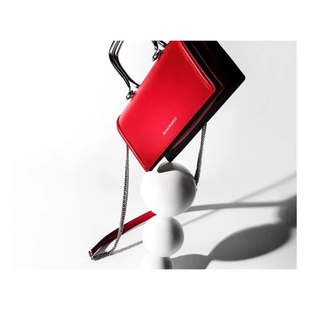 Red Alexander McQueen purse with chain handle, displayed against a white background with supporting white spherical pedestals.