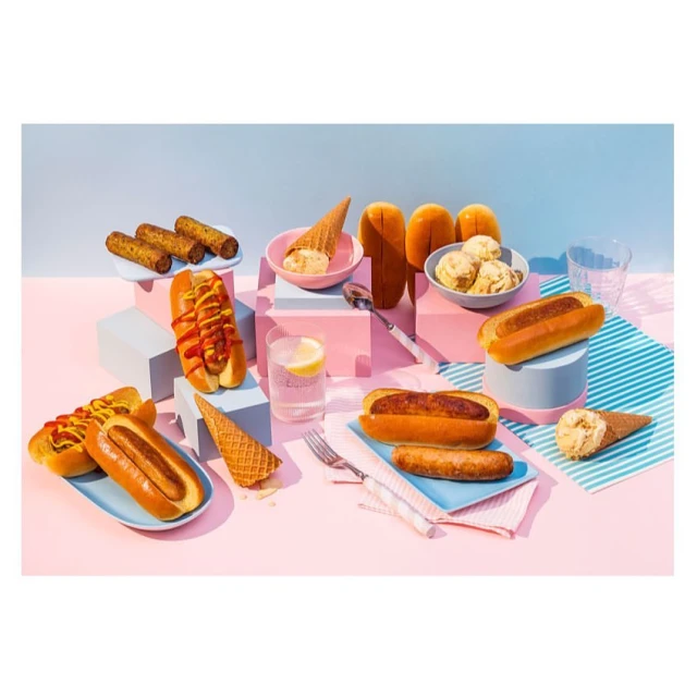 Whimsical still life featuring hot dogs, spring rolls, and ice cream cones arranged on pastel geometric platforms against a light blue backdrop.
