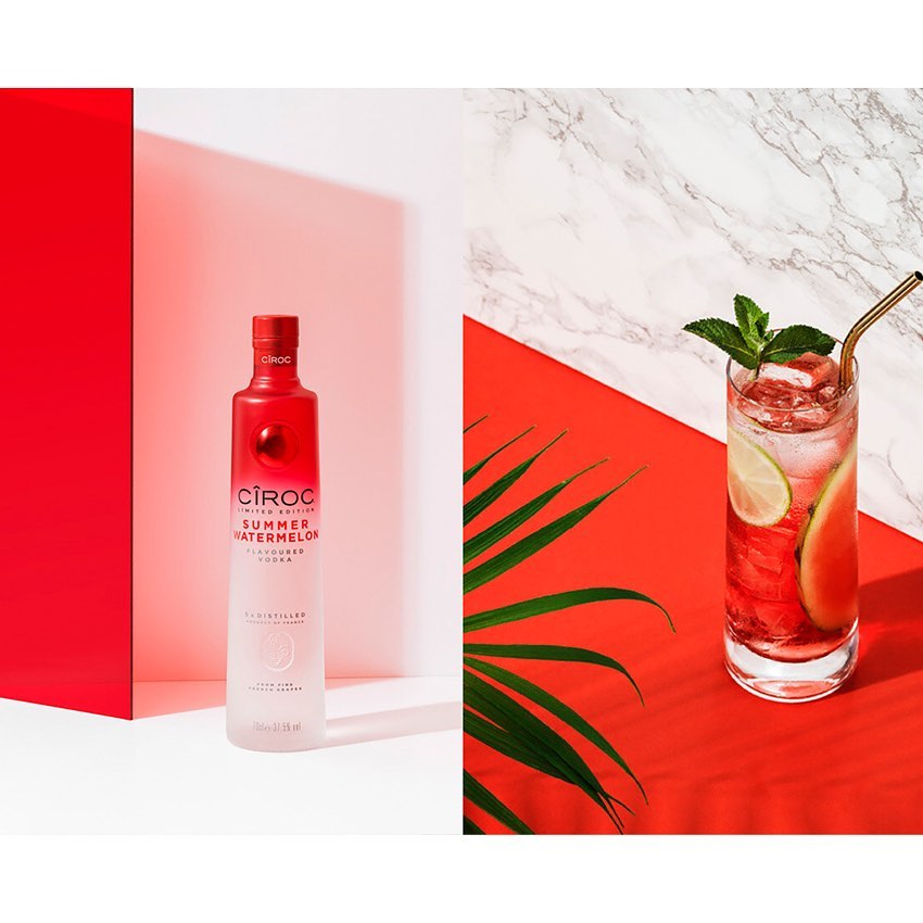 Studio shot of a Ciroc Summer Watermelon vodka bottle and a highball glass with watermelon cocktail against colorful studio background.